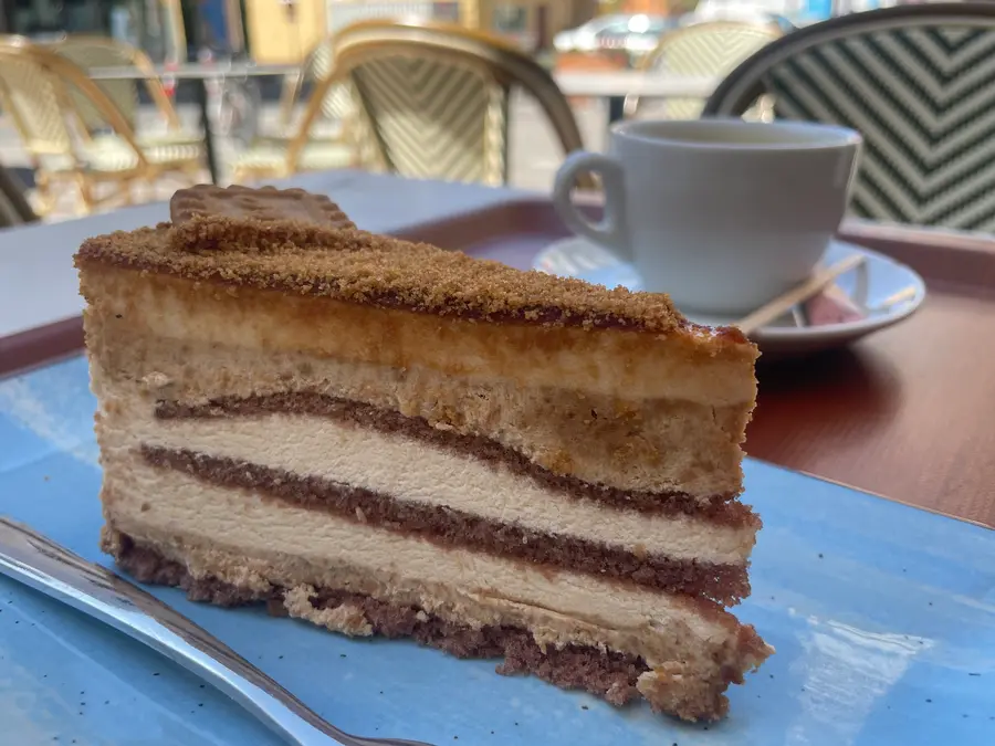Ein Stück Biscoff-Torte mit Keksbröseln, dahinter eine Tasse Kaffee auf der Terrasse