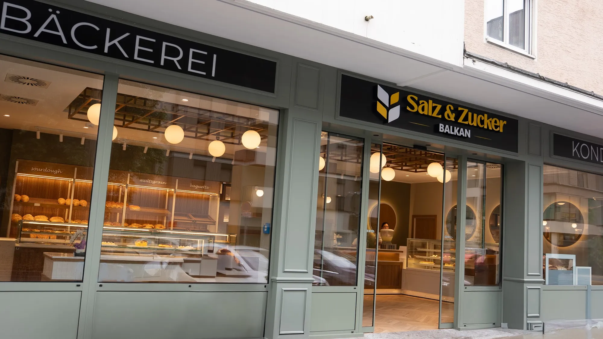 Die Fassade von Salz & Zucker in der Elisabethstraße: salbeigrüne Front, große Fenster, Schriftzug Bäckerei